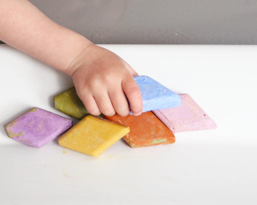 Little kid picking up bath crayons sitting on the side of the tub